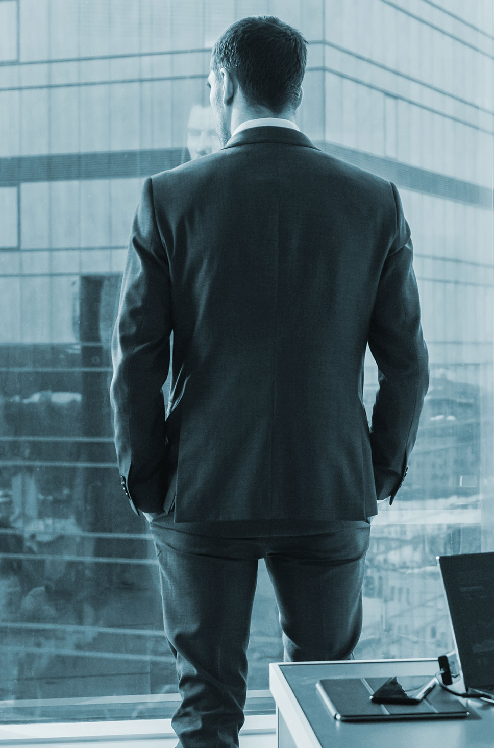 An image of a businessman with his back to the camera looking out the window of a skyscraper